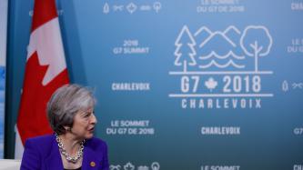 PM Theresa May sits in front of the Canadian flag.