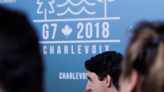 PM Trudeau sits in front the Charlevoix G7 Summit banner.