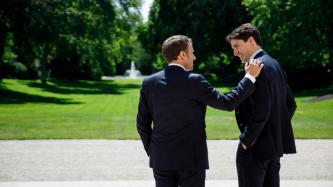 Le président Macron met sa main sur l’épaule du PM Trudeau alors que les deux sourient