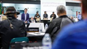 PM Trudeau sits on stage and looks at attendees
