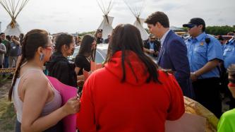 Le PM Trudeau parle à des femmes qui tiennent des affiches  