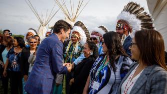 PM Trudeau shakes hands with a man in a headdress and speaks to a woman