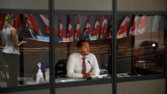 Un homme derrière une fenêtre écoute le PM Trudeau