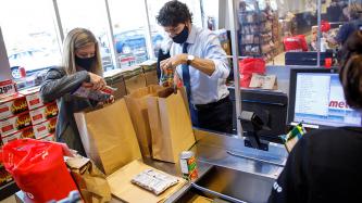 A woman and PM Trudeau bag groceries at a cash register