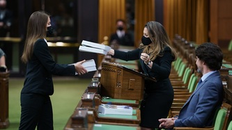 Deputy Prime Minister Chrystia Freeland hands books over to someone as Prime Minister Trudeau looks on