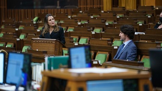 Deputy Prime Minister Chrystia Freeland stands at a podium looking at Prime Minister Justin Trudeau
