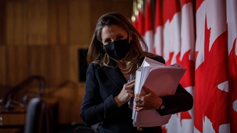 Deputy Prime Minister Chrystia Freeland holds papers and walks near a row of Canadian flags