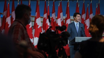 Le premier ministre Justin Trudeau, debout derrière un lutrin, fait face à des techniciens