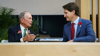 Michael Bloomberg and PM Trudeau look to one another at a table