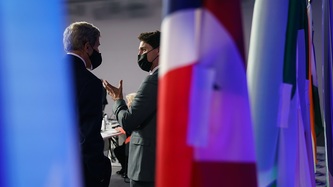 Prime Minister Justin Trudeau motions with his hand at a man as they stand near flags