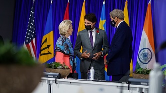 Ursula von der Leyen and John Kerry stand near PM Trudeau who motions with his hands
