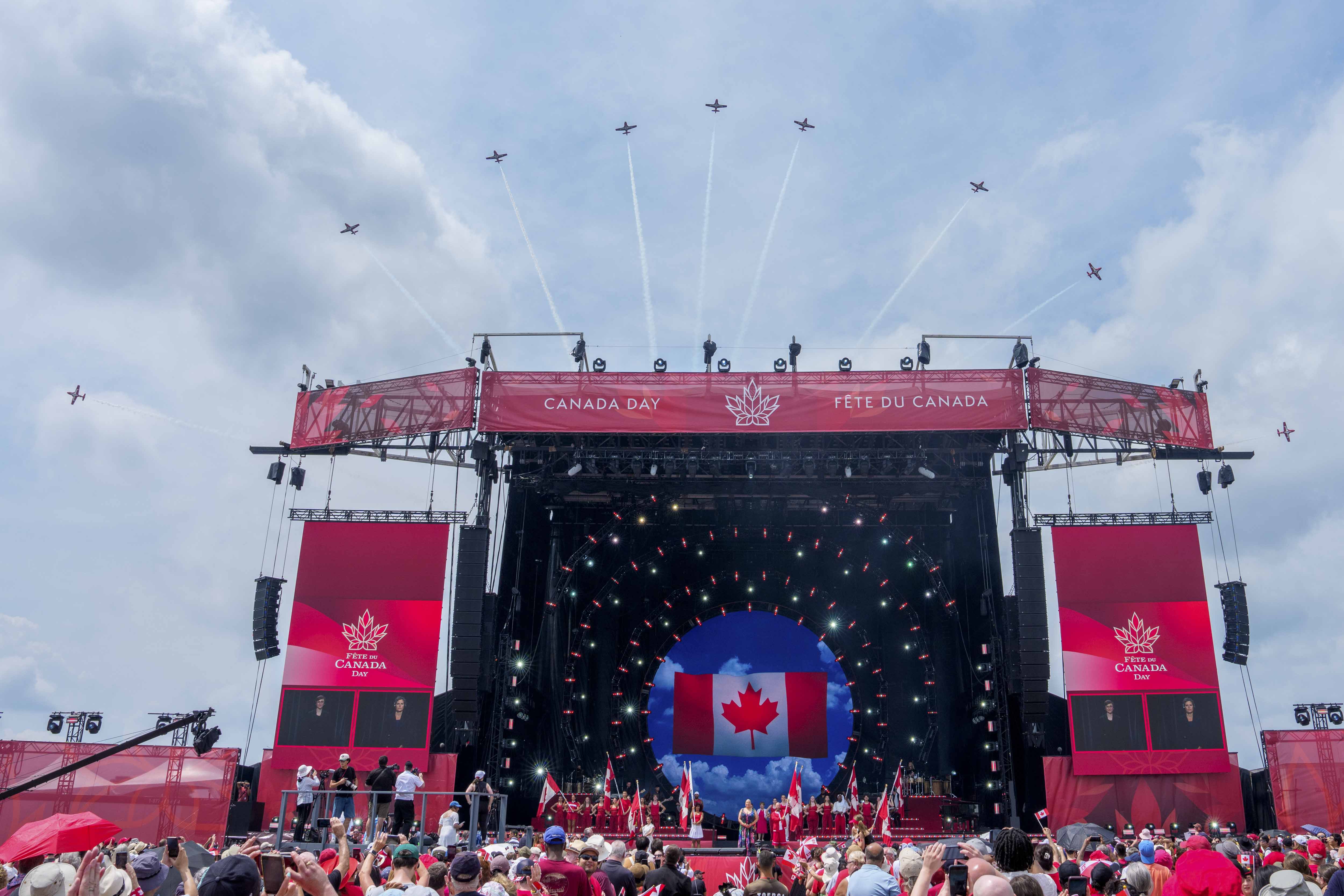 View of Snowbirds flying over the national Canada Day ceremony stage at LeBreton Flats Park.