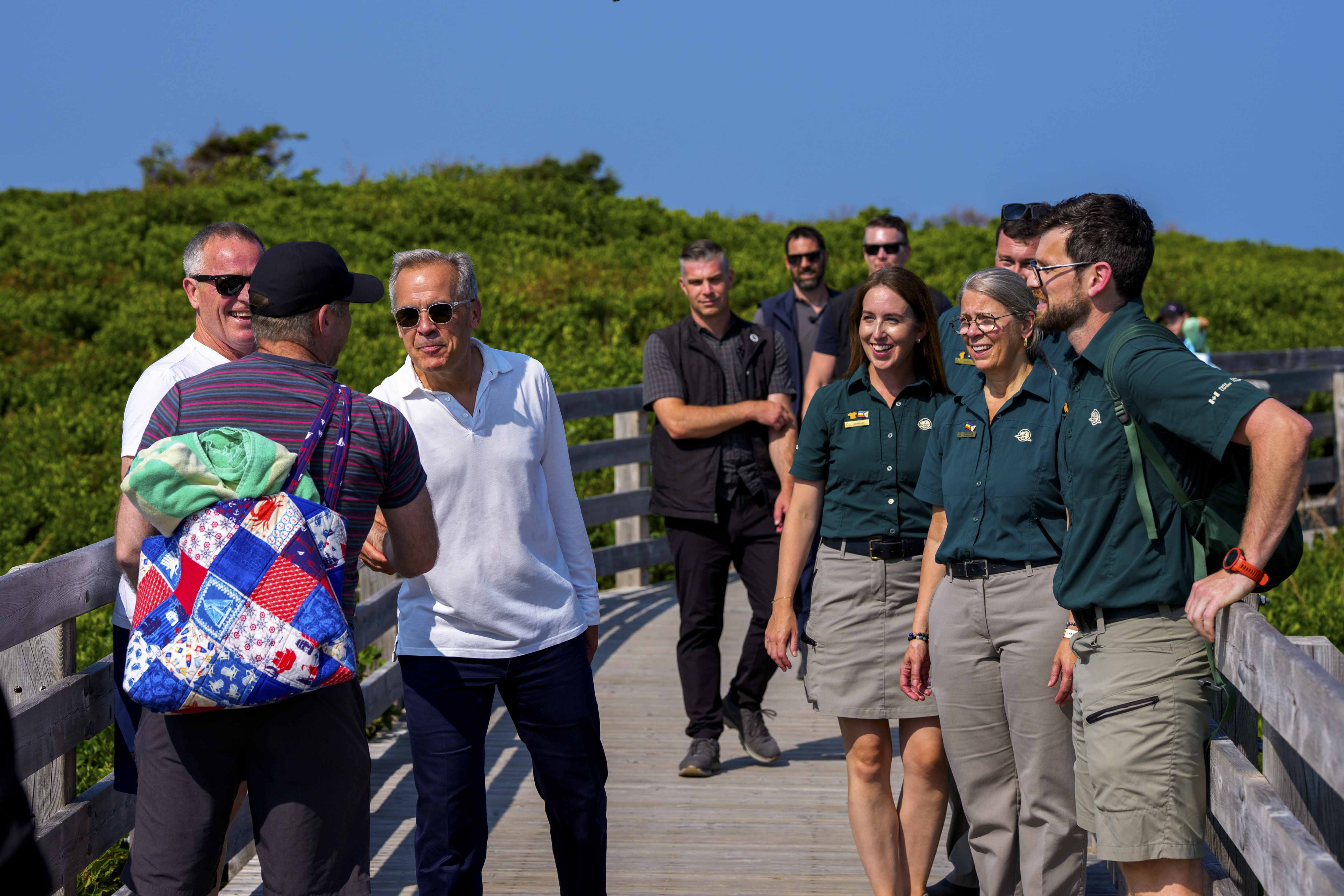 Prime Minister Mark Carney shakes hands with a man, as Parks Canada employees and others look on at PEI National Park.