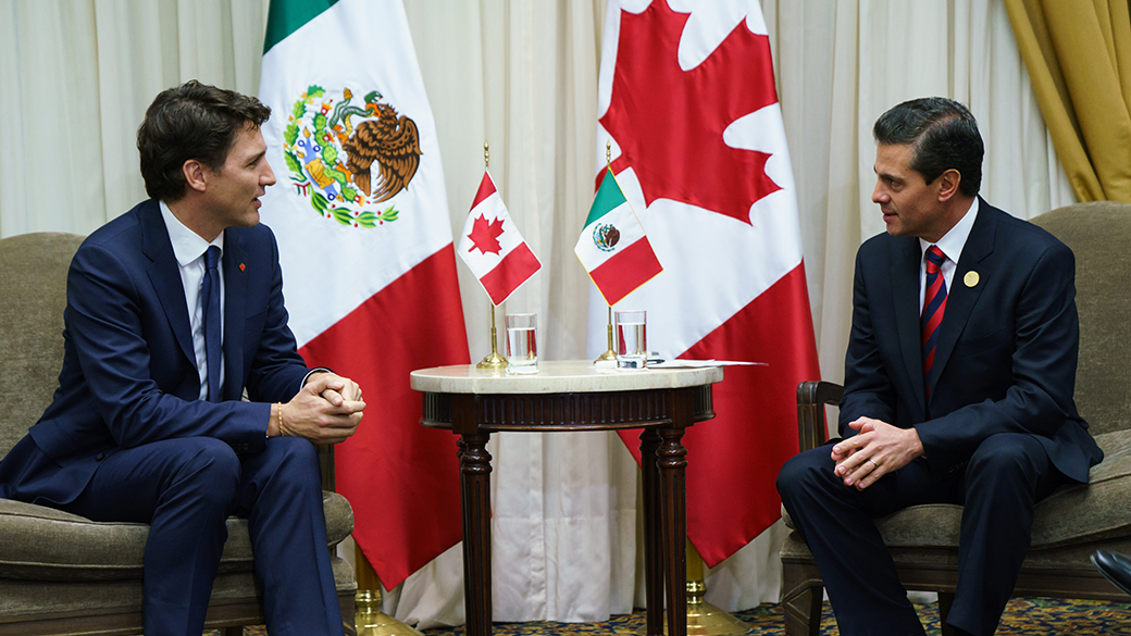 No title Prime Minister Justin Trudeau and President of Mexico Enrique Peña Nieto sit and talk in an office beside flags representing Canada and Mexico.