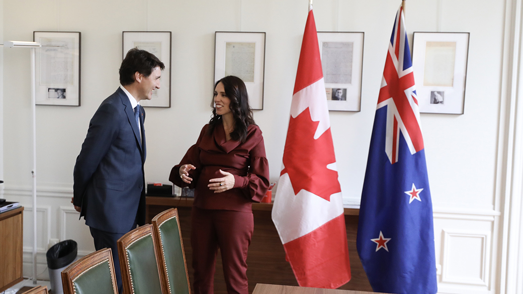 No title Prime Minister Justin Trudeau speaks with Prime Minister of New Zealand Jacinda Ardern in a room beside flags representing Canada and New Zealand.