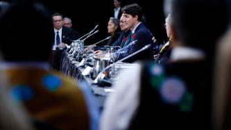 Prime Minister Justin Trudeau sits in front of a microphone and delivers remarks while officials and ministers look on