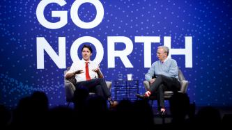 Prime Minister Justin Trudeau sits on the stage and speaks to the audience while Alphabet's Eric Schmidt looks on