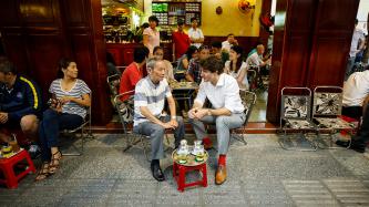Prime Minister Justin Trudeau sits and drinks coffee at a coffee shop with Nguyen Cong Hiep of the Canadian Consulate