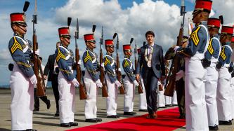 Prime Minister Justin Trudeau walks down a red carpet outside while military members stand at attention