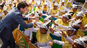 Prime Minister Justin Trudeau high fives a group of female performers in brightly coloured costumes