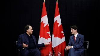 Prime Minister Justin Trudeau meets with Marc Benioff, Chairman and CEO of Salesforce beside two Canadian flags.
