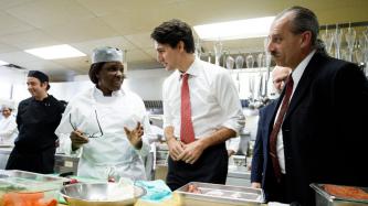 Prime Minister Justin Trudeau speaks to a chef at Cuisine-Atout in a kitchen while MP David Lametti and kitchen staff look on