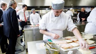 Prime Minister Justin Trudeau, MP Marc Miller and MP David Lametti watch a chef prepare food in the kitchen while another chef prepares sandwiches