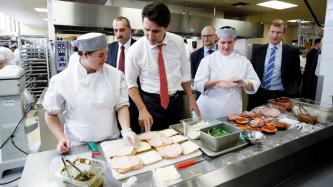 Prime Minister Justin Trudeau speaks with a chef preparing sandwiches in the kitchen, while MP Marc Miller and MP David Lametti and kitchen staff look on