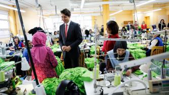 Prime Minister Justin Trudeau speaks to a female programme participant and Nahid Aboumansour, director general of Les Petites-Mains, while other participants work at sewing machines