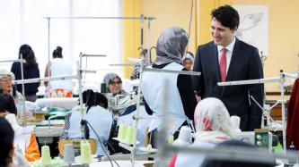 Prime Minister Justin Trudeau speaks to a female programme participant, while other participants work at sewing machines at Les Petites-Mains