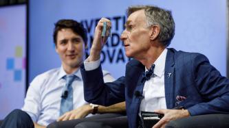 Bill Nye closely inspects a five dollar bill while Prime Minister Justin Trudeau looks on during an armchair discussion at the University of Ottawa