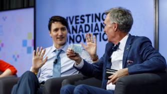 Bill Nye holds up a five dollar bill while Prime Minister Justin Trudeau looks on during an armchair discussion at the University of Ottawa