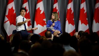 Prime Minister Justin Trudeau gestures during an armchair discussion hosted by Tanya van Biesen, Executive Director of Catalyst Canada, with a row of Canadian flags in the background.