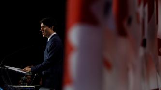Prime Minister Justin Trudeau delivers remarks from a podium in front of a row of Canadian flags.