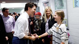 Prime Minister Justin Trudeau shakes hands with a young girl in a hallway of the Stronach Aurora Recreation Complex as others look on