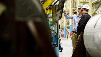 Prime Minister Justin Trudeau pointing at a panel and speaking with an ArcelorMittal Dofasco employee