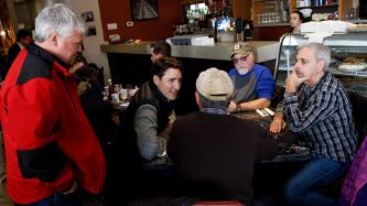 Prime Minister Justin Trudeau sits and talks with customers of Muio's Restaurant while MP Terry Sheehan stands at his side