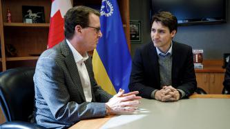 Prime Minister Justin Trudeau and mayor of Regina, Michael Fougere, have a discussion in an office beside flags representing Canada and Regina
