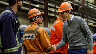 Prime Minister Justin Trudeau wears a hard hat and safety goggles and shakes hands with an EVRAZ Regina employee