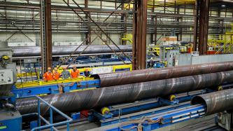 Prime Minister Justin Trudeau and Minister Ralph Goodale wear hard hats and safety goggles as they look at large pipes and machinery during a tour of the EVRAZ Regina facility with three uniformed employees