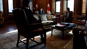 Prime Minister Justin Trudeau and two staff smile while seated in his office.