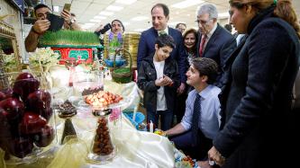 A young boy speaks to Prime Minister Trudeau in front of a seasonal display of food items surrounded by on-lookers at the Parsian Fine Foods grocery store.