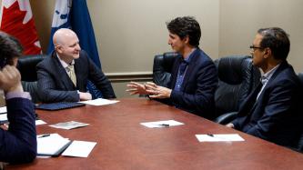 Prime Minister Justin Trudeau sits and speaks with Mayor Don Scott during a meeting while Minister Amarjeet Sohi looks on 