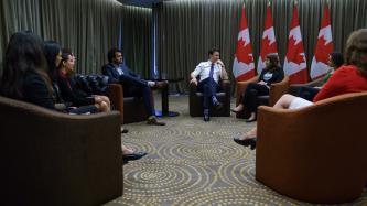 Prime Minister Justin Trudeau and Canadian youth delegates to the Young Americas Forum sit in arm chairs in front of Canadian flags