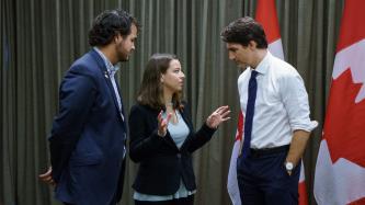 A couple of Canadian youth delegates to the Young Americas Forum speak to Prime Minister Justin Trudeau, who stands with his hands in his pockets while listening 