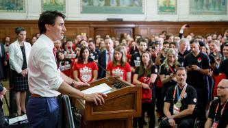 Prime Minister Justin Trudeau stands at a podium and speaks to a group of Olympians and Paralympians in Parliament