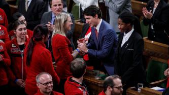 Prime Minister Justin Trudeau shakes hands and speaks to a female athlete in the House of Commons while other MPs and athletes look on