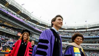 Prime Minister Justin Trudeau walks on to the field at Yankee Stadium flanked by two women, all in doctoral regalia