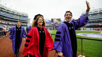 Prime Minister Justin Trudeau smiles and waves to the crowd while walking with others in doctoral regalia on the field at Yankee Stadium