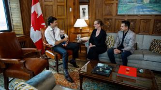Prime Minister Justin Trudeau sits across from Minister Karina Gould and her partner Alberto Gerones holding their baby